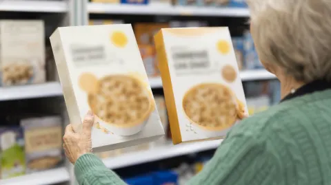 Hands comparing two boxes of cereal in a grocery aisle