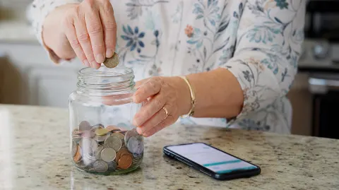 Hands dropping coins into a glass savings jar